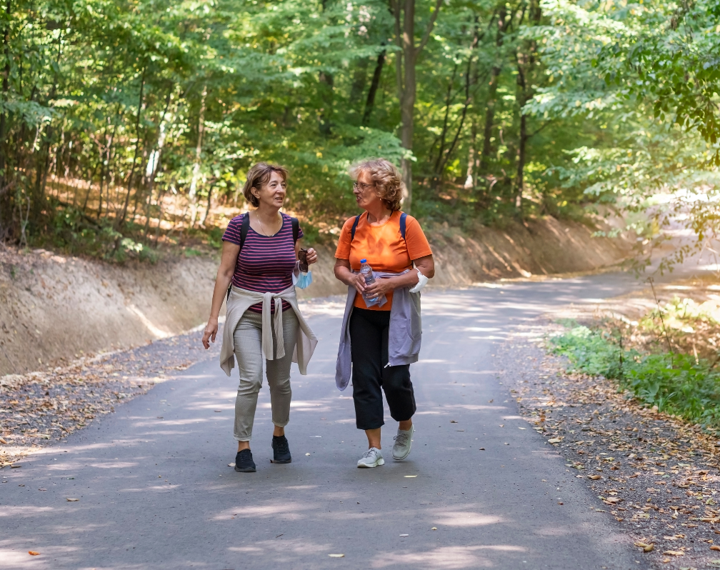 image shows two middle aged women chatting and walking together on a path. Set in nature and woodland.