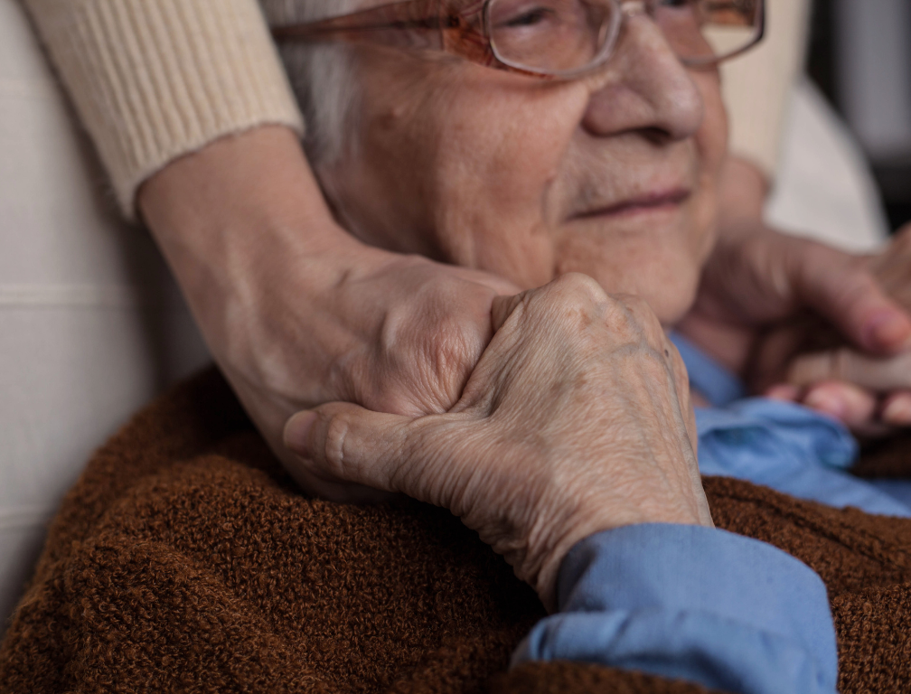 image shows an older person being comforted by the hand of a carer or family member