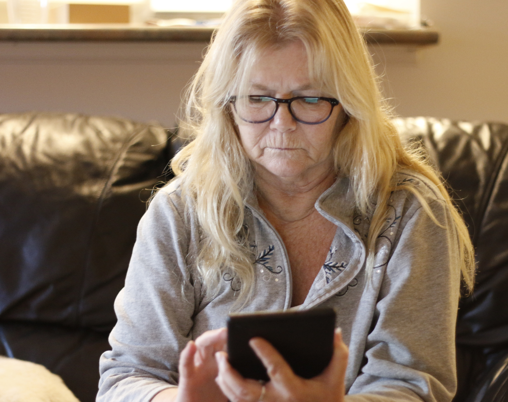 photo shows an older lady sat on a sofa using her mobile phone